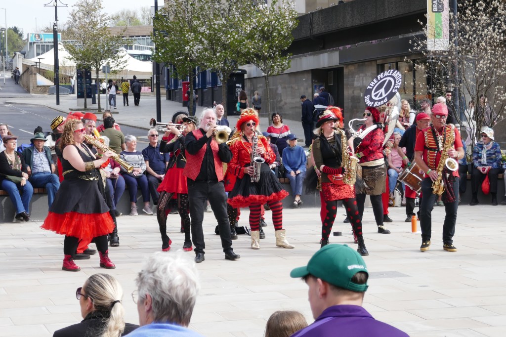 A lively street performance featuring a brass band dressed in vibrant costumes, playing music outdoors in front of an audience.